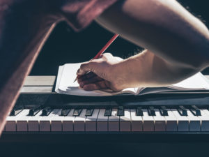 A man plays the piano and writes in a notebook in the dark.